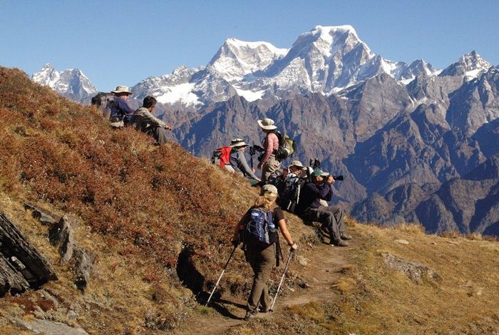 This may contain: a group of people hiking up the side of a mountain with snow capped mountains in the background