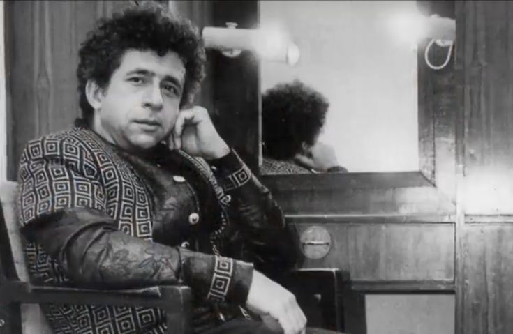 This may contain: a black and white photo of a man sitting in a chair talking on the phone