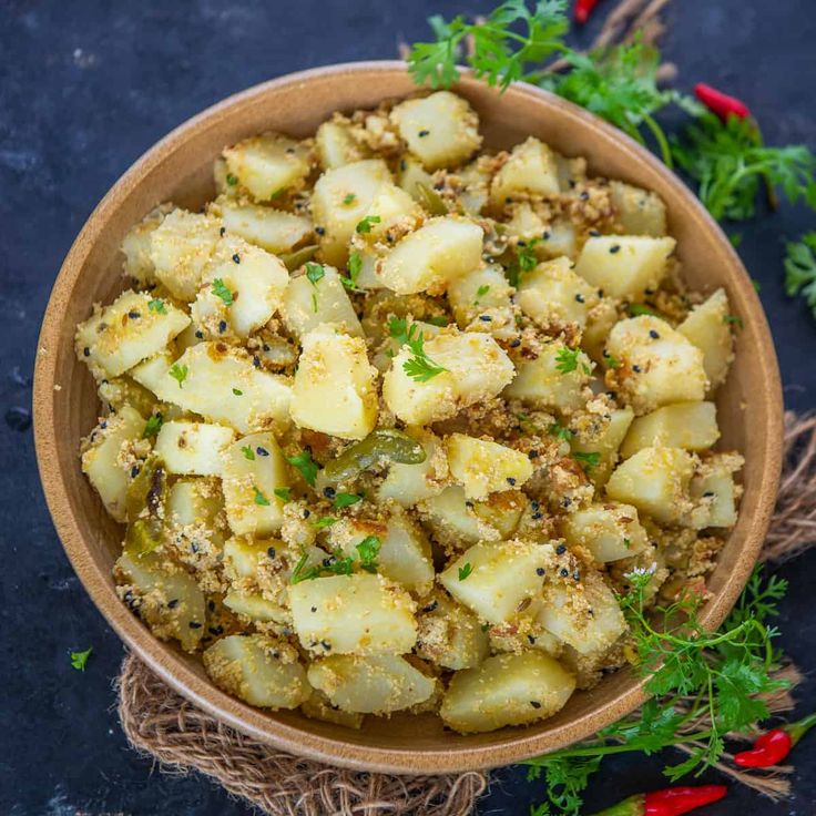 This may contain: a bowl filled with potatoes and herbs on top of a blue tablecloth next to red peppers
