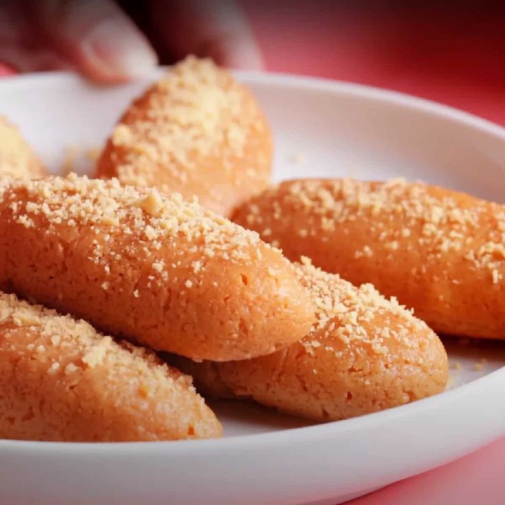 This may contain: some sugared donuts are in a white bowl on a pink tablecloth with someone's hand